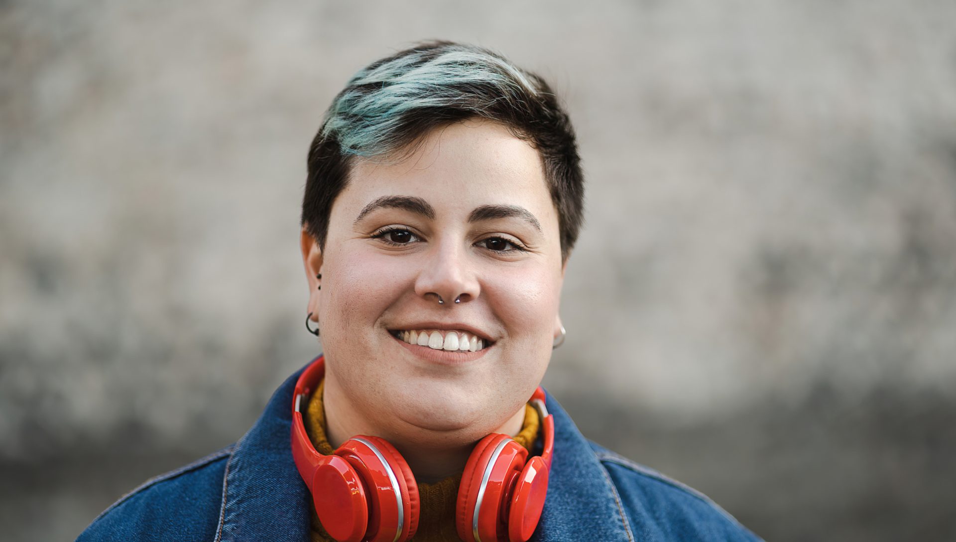 a woman with short hair and dark eyes is wearing red headphones while standing outside and smiling at the camera
